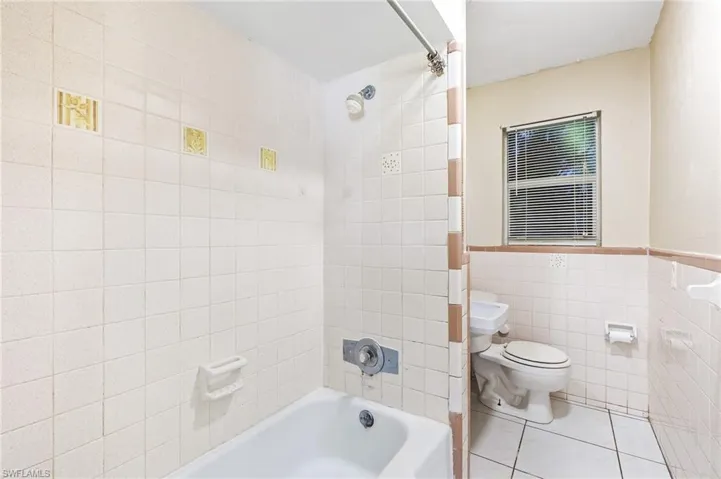 Full bath featuring tile walls, tile patterned floors, shower / washtub combination, and a wainscoted wall