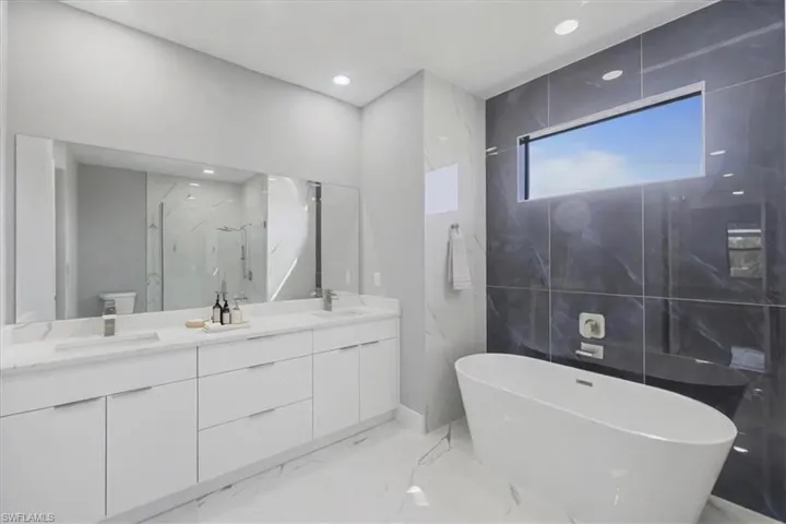 Bathroom with marble tiled floors, a marble finish shower, double vanity, a soaking tub, and recessed lighting