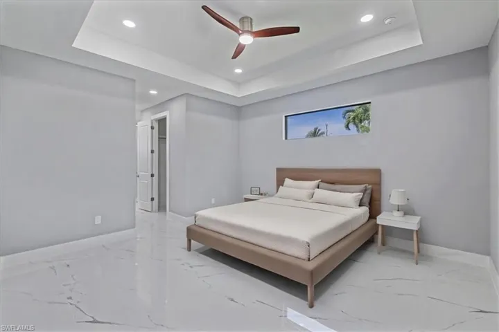 Bedroom with recessed lighting, light marble finish flooring, a tray ceiling, and ceiling fan