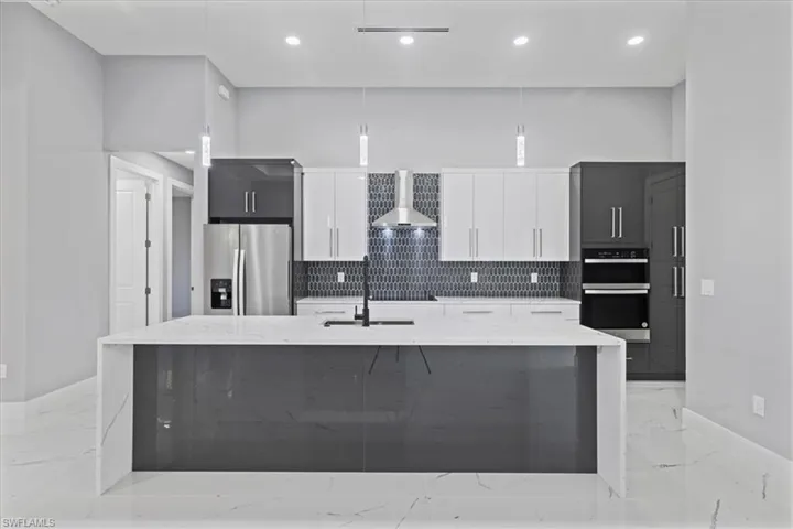 Kitchen with stainless steel fridge with ice dispenser, wall chimney range hood, double wall oven, light marble finish flooring, and recessed lighting