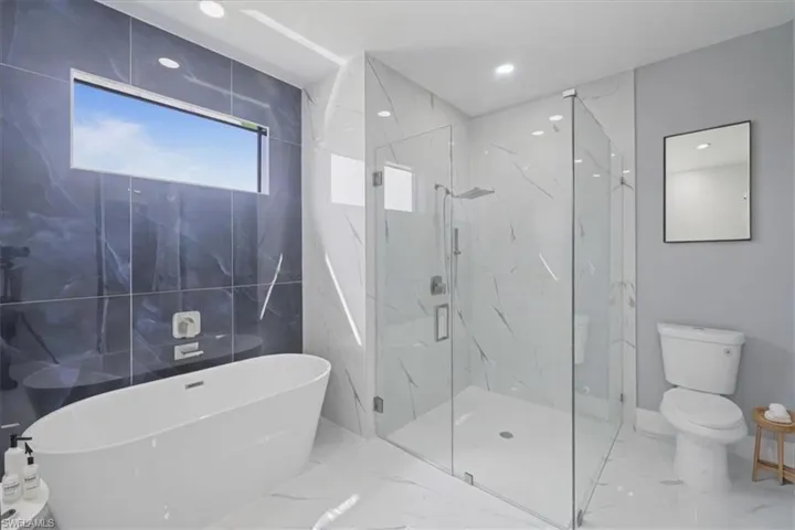 Full bathroom featuring marble tiled flooring, a freestanding bath, a marble finish shower, and recessed lighting