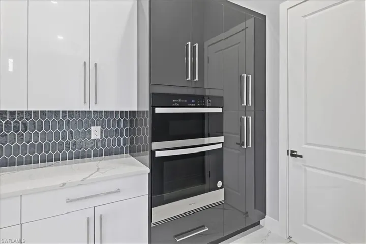 Kitchen with stainless steel double oven, light stone countertops, white cabinets, tasteful backsplash, and marble finish floors