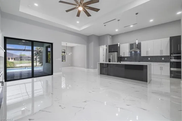 Kitchen featuring stainless steel fridge, modern cabinets, wall chimney range hood, decorative backsplash, and light countertops
