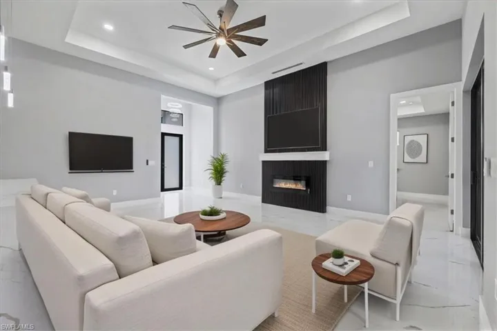 Living room featuring a raised ceiling, light marble finish floors, ceiling fan, recessed lighting, and a fireplace