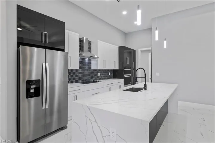 Kitchen with appliances with stainless steel finishes, wall chimney exhaust hood, modern cabinets, an island with sink, and light marble finish flooring