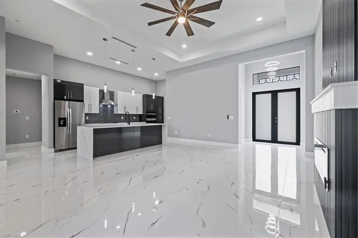 Kitchen with stainless steel fridge, modern cabinets, a ceiling fan, light marble finish floors, and backsplash