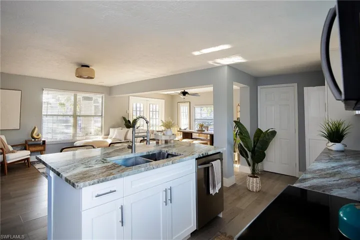 Kitchen with white cabinets, open floor plan, dark wood finished floors, light stone counters, and a kitchen island with sink