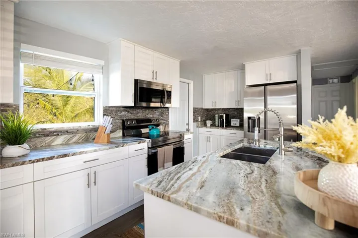Kitchen with stainless steel appliances, white cabinets, light stone countertops, and a textured ceiling
