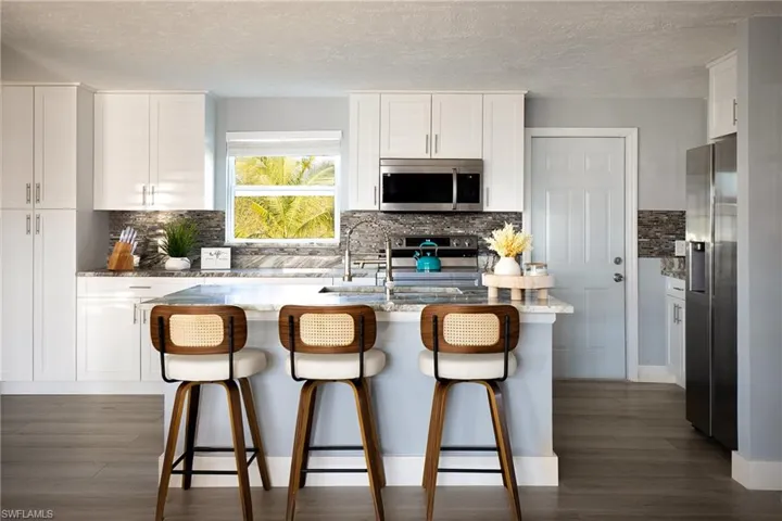 Kitchen with stainless steel appliances, light stone countertops, backsplash, dark wood finished floors, and a textured ceiling