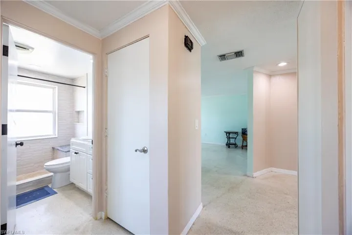 Hallway featuring light speckled floor, baseboards, ornamental molding, and visible vents