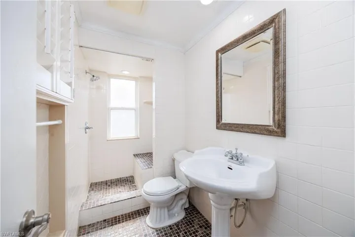 Bathroom featuring toilet, tile walls, ornamental molding, and a shower stall