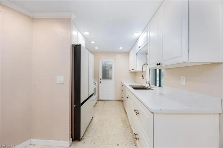Kitchen with freestanding refrigerator, recessed lighting, light countertops, white cabinetry, and a sink