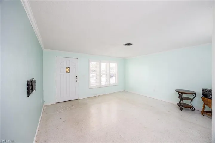 Foyer entrance with crown molding, baseboards, visible vents, and speckled floor