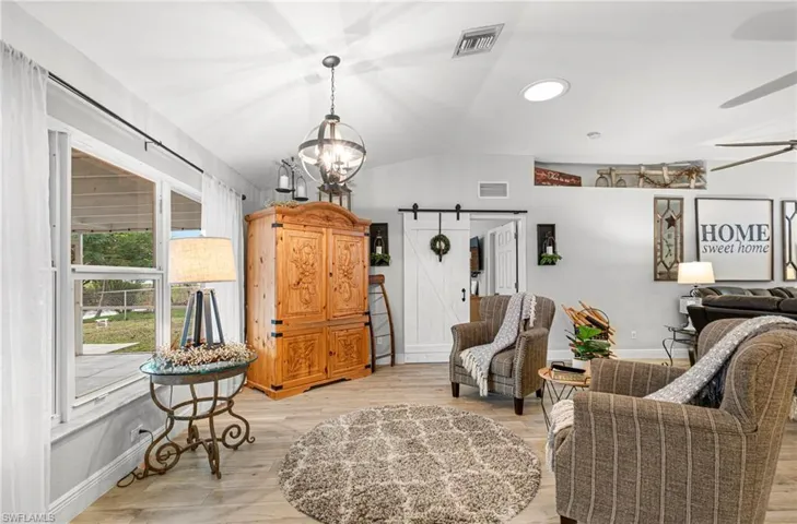 Living area with a barn door, lofted ceiling, light wood-type flooring, and a chandelier