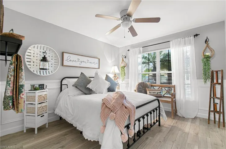 Bedroom with a wainscoted wall, a decorative wall, light wood-type flooring, and ceiling fan