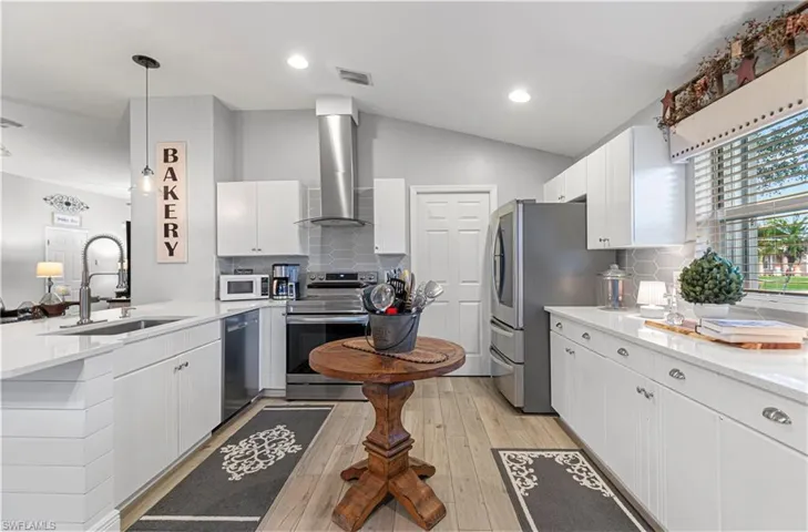 Kitchen featuring white cabinets, appliances with stainless steel finishes, light stone counters, decorative light fixtures, and vaulted ceiling