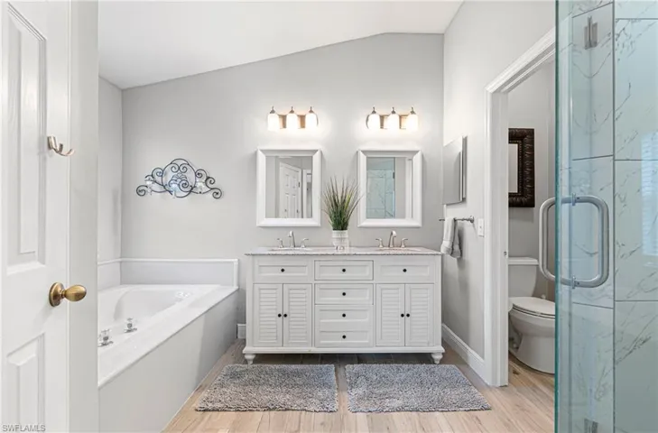 Full bathroom featuring double vanity, lofted ceiling, light wood-style floors, a marble finish shower, and a garden tub