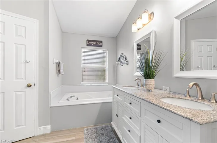 Bathroom with double vanity, light wood-type flooring, and a bath