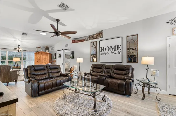 Living area with a barn door, lofted ceiling, light wood-style floors, and a ceiling fan