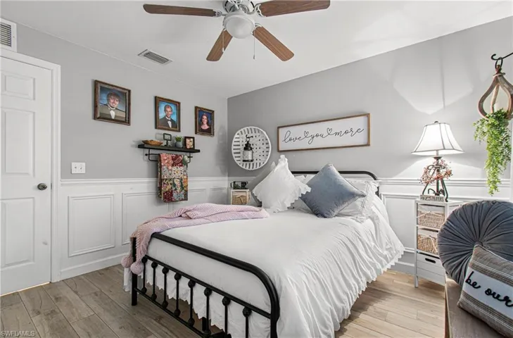 Bedroom featuring wainscoting, hardwood / wood-style flooring, a decorative wall, and a ceiling fan