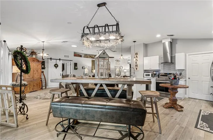 Dining area with a barn door, light wood-type flooring, lofted ceiling, and recessed lighting