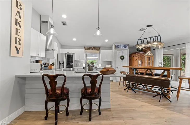 Kitchen featuring hanging light fixtures, a peninsula, white cabinetry, stainless steel fridge, and recessed lighting