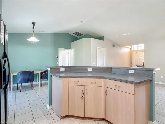 Kitchen featuring light brown cabinetry, light tile patterned flooring, dark countertops, decorative light fixtures, and a center island