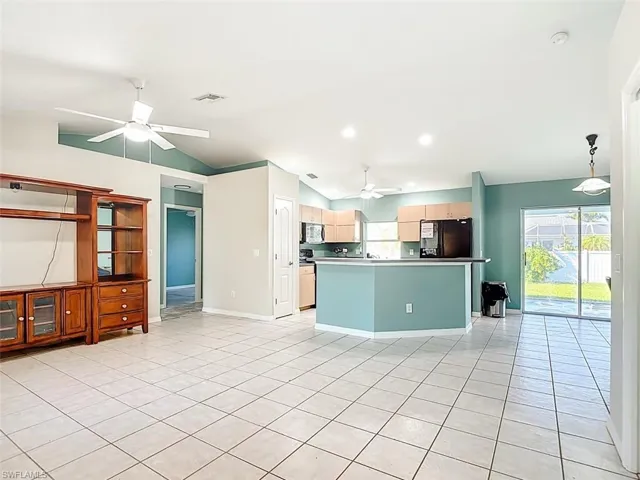 Kitchen with vaulted ceiling, ceiling fan, freestanding refrigerator, light tile patterned flooring, and plenty of natural light