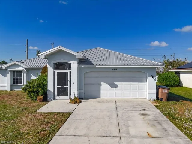 Ranch-style home featuring a metal roof, stucco siding, a front lawn, and concrete driveway