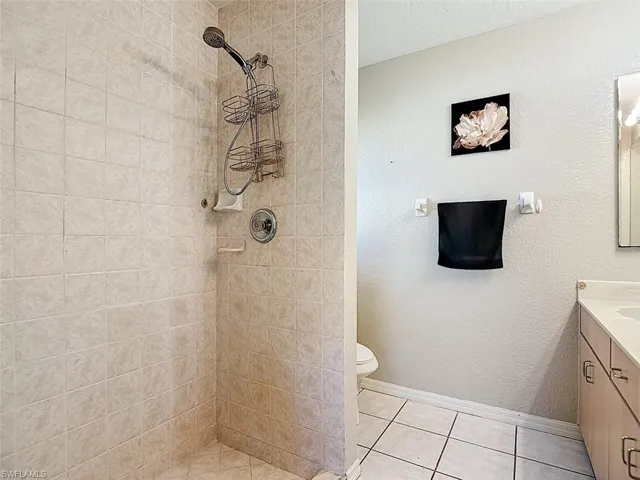 Full bath with vanity, tiled shower, a textured wall, light tile patterned floors, and a textured ceiling