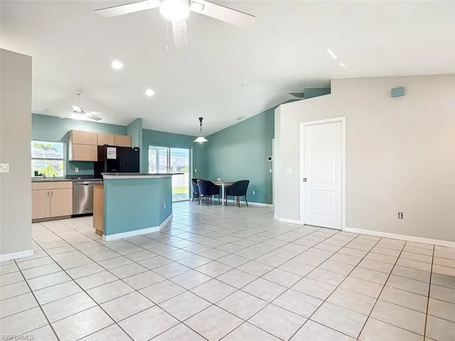 Kitchen with light brown cabinetry, vaulted ceiling, hanging light fixtures, freestanding refrigerator, and light tile patterned floors