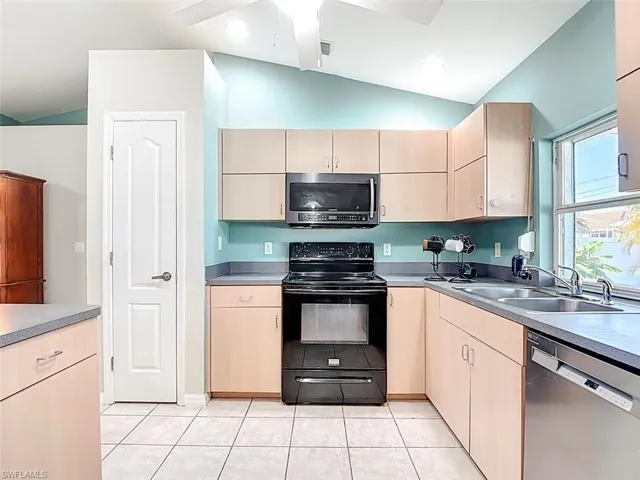 Kitchen with appliances with stainless steel finishes, light brown cabinetry, lofted ceiling, and light tile patterned floors