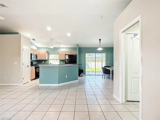 Kitchen featuring freestanding range oven, black refrigerator with ice dispenser, light tile patterned flooring, recessed lighting, and stainless steel microwave