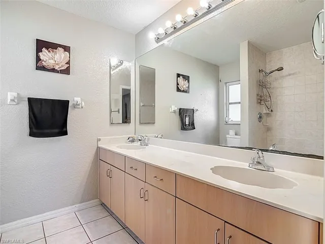 Bathroom with a textured ceiling, double vanity, a textured wall, light tile patterned floors, and tiled shower