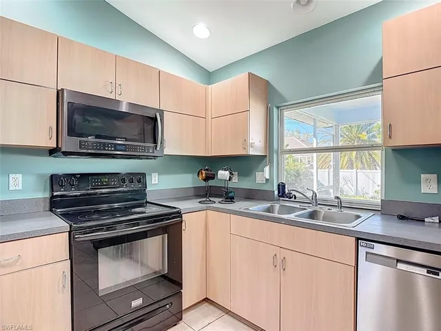 Kitchen featuring light brown cabinets, stainless steel appliances, lofted ceiling, light tile patterned floors, and recessed lighting