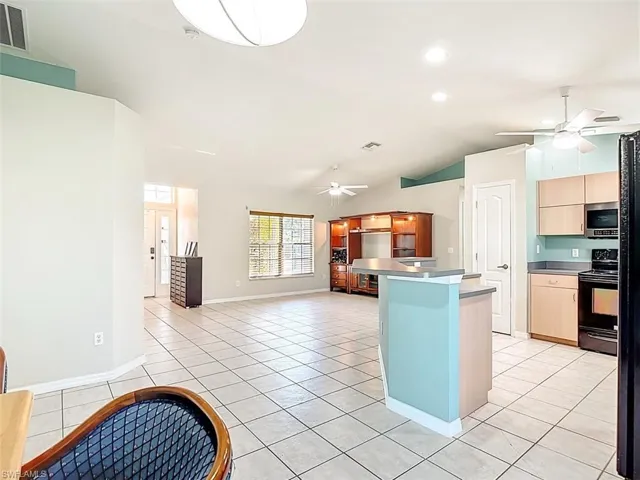 Kitchen featuring black appliances, lofted ceiling, light brown cabinetry, a ceiling fan, and light tile patterned floors