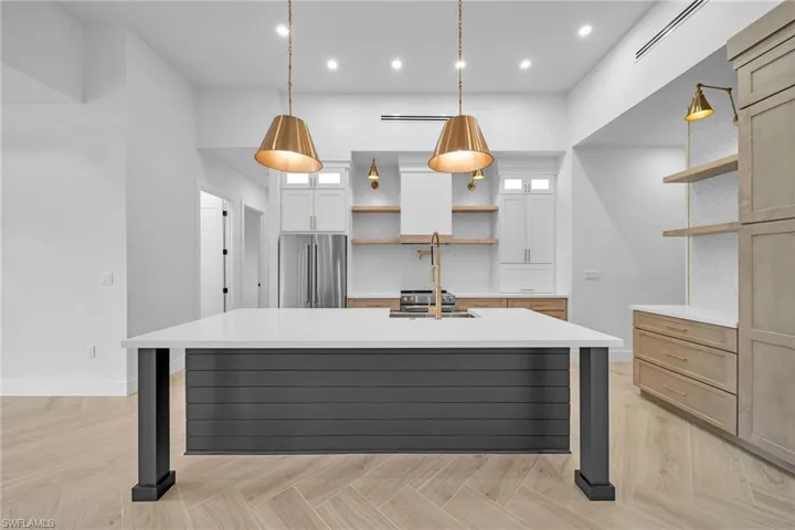 Kitchen featuring pendant lighting, a large island with sink, white cabinetry, stainless steel refrigerator, and light parquet floors