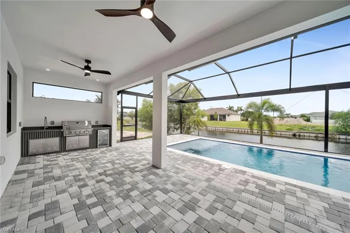 View of swimming pool featuring a patio, a water view, area for grilling, glass enclosure, and ceiling fan