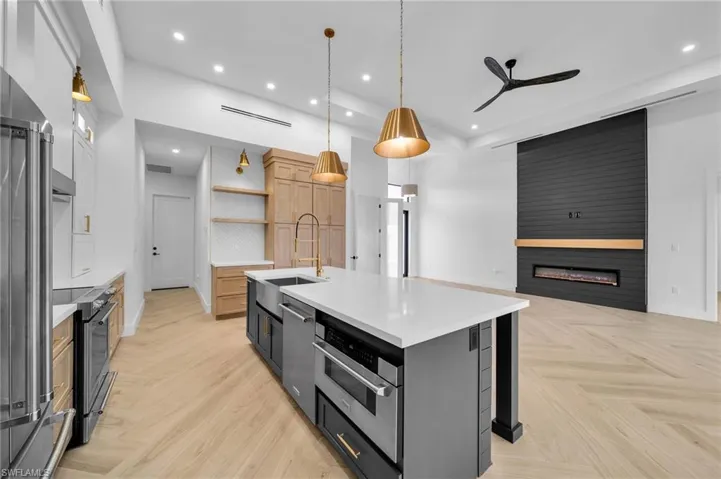 Kitchen with pendant lighting, an island with sink, appliances with stainless steel finishes, light brown cabinets, and a large fireplace