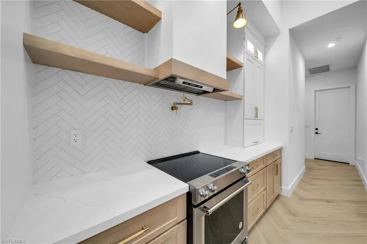 Kitchen featuring decorative backsplash, light stone counters, light parquet flooring, high end stove, and premium range hood