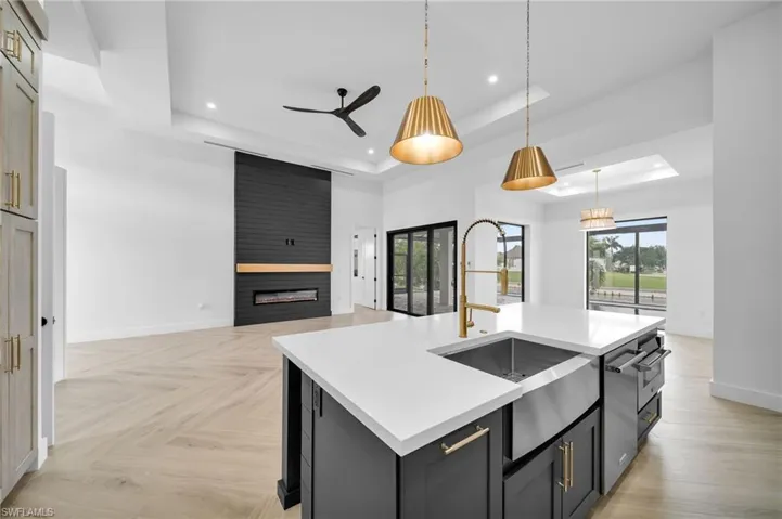 Kitchen with a tray ceiling, hanging light fixtures, a fireplace, a center island with sink, and light parquet floors