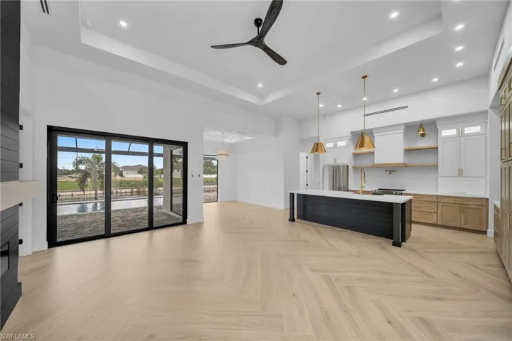 Kitchen featuring white cabinetry, decorative light fixtures, a raised ceiling, and a large island with sink