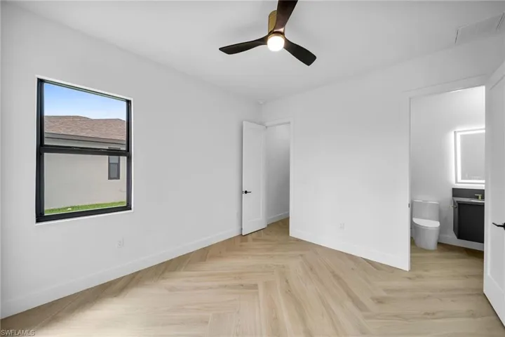 Unfurnished bedroom featuring ensuite bath, ceiling fan, and light parquet flooring