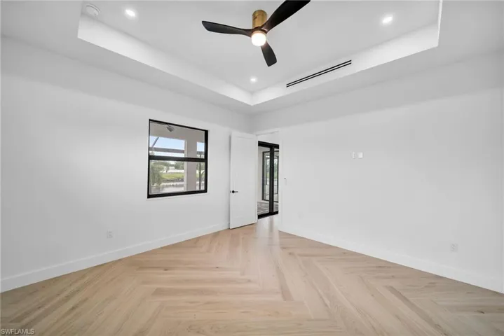 Empty room with a raised ceiling, light parquet flooring, and ceiling fan