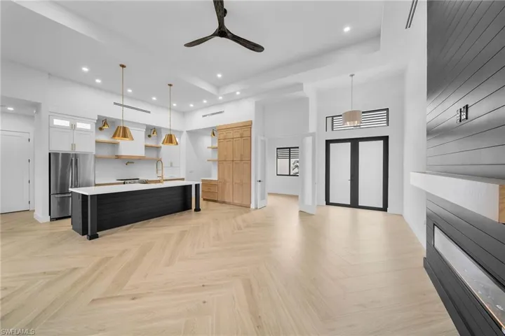Kitchen with hanging light fixtures, white cabinetry, light parquet flooring, stainless steel refrigerator, and a center island with sink