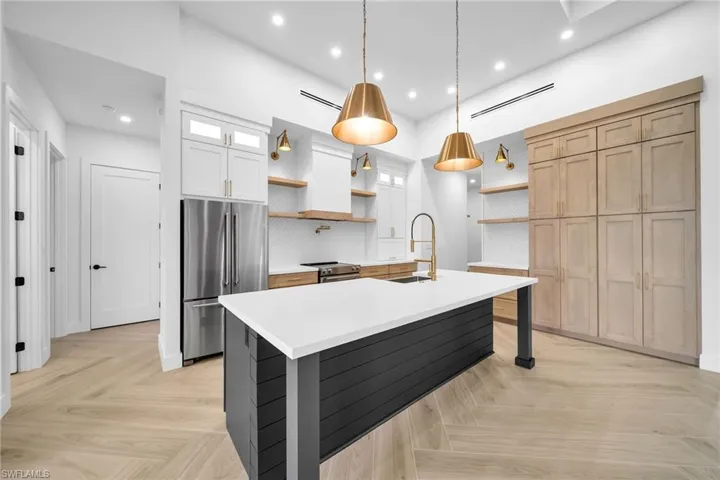 Kitchen with tasteful backsplash, white cabinets, light parquet flooring, appliances with stainless steel finishes, and decorative light fixtures