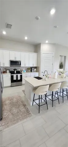 Kitchen featuring visible vents, white cabinetry, appliances with stainless steel finishes, light countertops, and a breakfast bar area