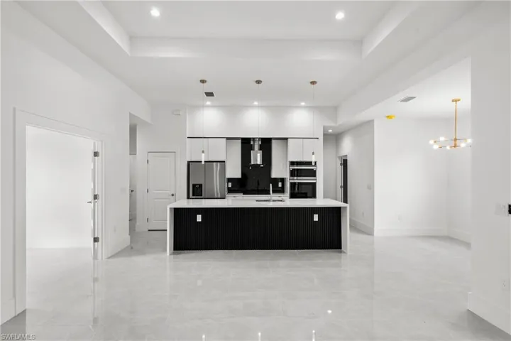 Kitchen featuring large island with sink, white cabinets, stainless steel appliances, modern cabinets.