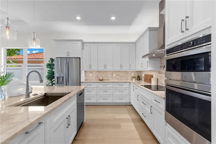 Kitchen featuring light stone counters, backsplash, light wood-type flooring, appliances with stainless steel finishes, and sink