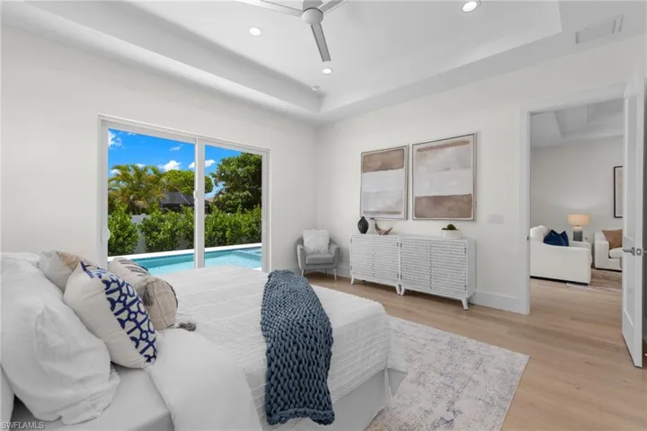Bedroom with a tray ceiling, ceiling fan, light hardwood / wood-style floors, and access to outside